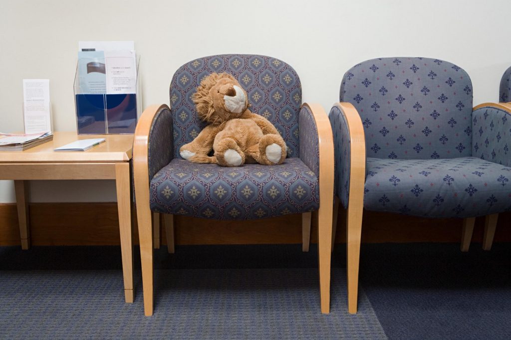 Fotografie a unei săli de așteptare în care pe un scaun este un ursuleț de pluș pentru copii